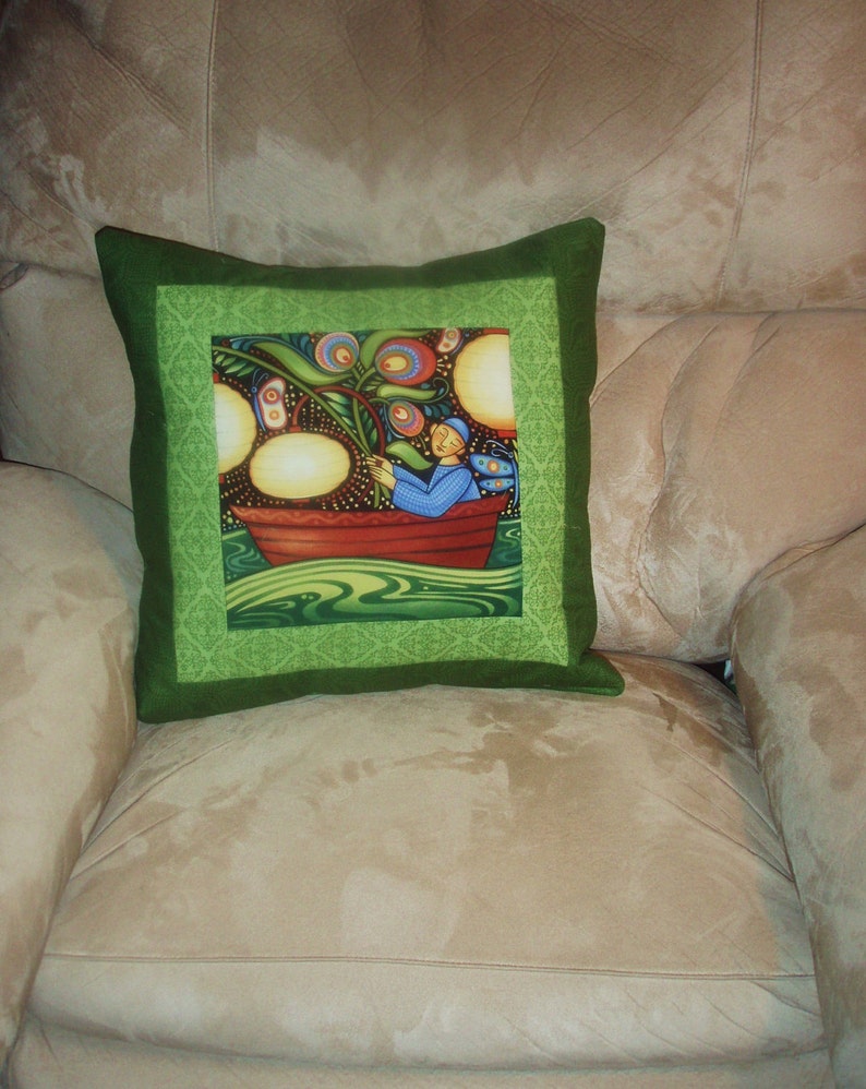 May include: Green pillow with a colorful illustration of a person in a boat surrounded by flowers and a green background.