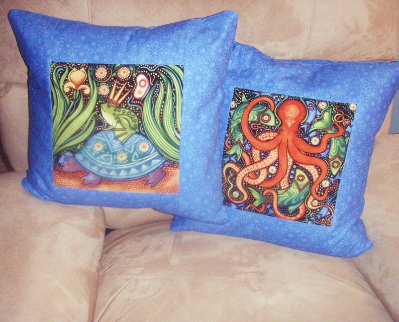 Puede incluir: Dos fundas de coj&iacute;n azules con dise&ntilde;os bordados coloridos. Una funda de coj&iacute;n presenta una rana verde con una corona montada en una tortuga azul. La otra funda de coj&iacute;n presenta un pulpo rojo con algas verdes y peces.
