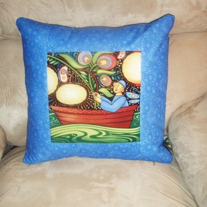 Puede incluir: Almohada azul con un dise&ntilde;o floral colorido y una persona en un bote en la parte delantera. El bote es rojo y la persona lleva una camisa azul. El fondo es verde y azul.