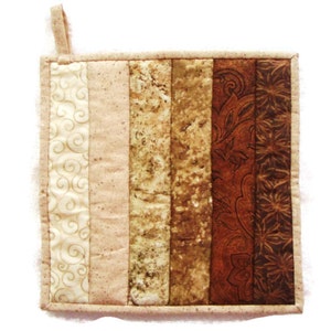 May include: A brown and beige quilted pot holder with a hanging loop. The pot holder is made of fabric with different patterns, including swirls, stripes, and paisley.