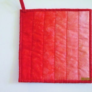 May include: Red quilted hot pad with a hanging loop. The pad is made of a gradient fabric with shades of red, pink, and white. The date 09/01/2012 is written in the bottom right corner.