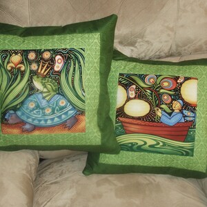 May include: Two green pillow covers with a green border. One pillow features a frog wearing a crown riding a turtle. The other pillow features a person in a boat with a flower and lights.