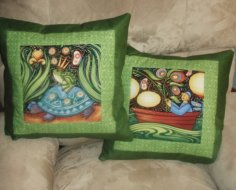 May include: Two green pillow covers with a green border. One pillow features a frog wearing a crown riding a turtle. The other pillow features a person in a boat with a flower and lights.