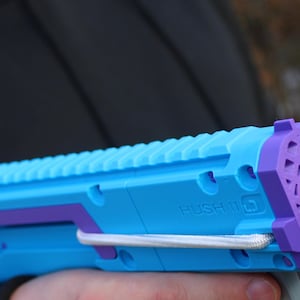 May include: A blue and purple toy gun with an orange barrel. The gun has a textured grip and the words "Hush MG" printed on the side.