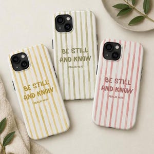May include: Three phone cases with vertical striped patterns in yellow, green, and pink. Each case features the text "BE STILL AND KNOW" and "PSALM 46:10" in a complementary color to the stripes. The cases are for a smartphone.