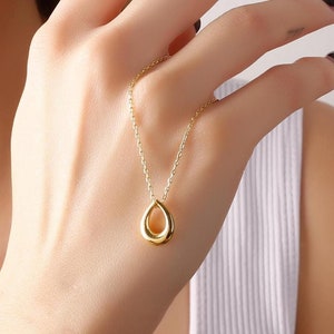 May include: A gold necklace with a teardrop-shaped pendant. The pendant is hollow and has a smooth, polished finish.