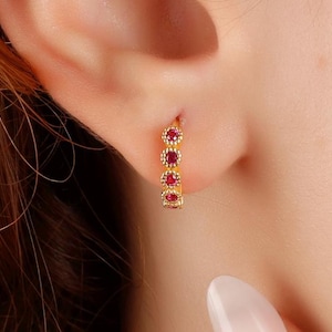 May include: Gold hoop earrings with a row of small red gemstones.