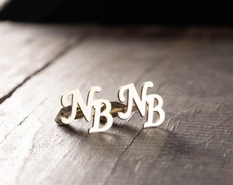 May include: A pair of gold-toned cufflinks with the letters "NB" in a cursive font.