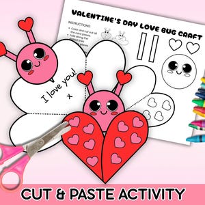 Puede incluir: Un kit de manualidades para el Día de San Valentín con un diseño de mariquita rosa y roja. El kit incluye una hoja imprimible con instrucciones, una mariquita recortable y unas tijeras rosas. Se ven crayones a la derecha. El texto "I love you!" está escrito en la manualidad.