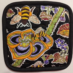 May include: Black quilted hot pad with a floral design featuring bees and flowers. The flowers are purple, orange, and green. The bees are yellow and black.