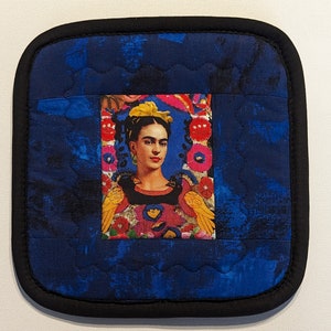 Puede incluir: Un posavasos acolchado azul con borde negro presenta una imagen colorida de Frida Kahlo en el centro.
