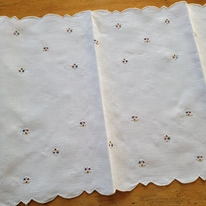 Peut inclure: Tissu blanc brodé avec un bord festonné et un motif répétitif de petites fleurs colorées.