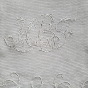 Può includere: Tessuto bianco ricamato con un bordo a festoni e il monogramma "KBF" in un carattere corsivo.