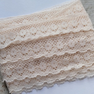 May include: A roll of cream-coloured lace. The lace has a scalloped edge and a floral pattern. The lace is tightly woven and appears to be made of a soft, natural fibre. Suitable for sewing, crafting, and adding a vintage touch to projects.