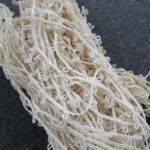 Puede incluir: Primer plano de un montón de ribete de encaje hecho a mano de color blanquecino. El ribete presenta un diseño de bucles a lo largo de los bordes, creando una apariencia delicada y texturizada. El encaje probablemente está hecho de algodón o una fibra natural similar.