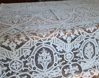 May include: A white lace tablecloth with an intricate floral and geometric pattern. The delicate openwork design covers the entire surface, creating a textured and elegant look. This decorative textile is suitable for special occasions or everyday use.