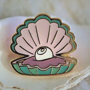 May include: A gold-tone enamel pin featuring a pink seashell with a white pearl inside. The shell has a green and blue border.