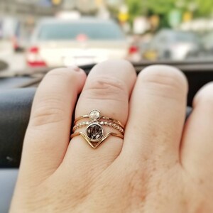 May include: A gold ring with three bands and a clear stone in the centre. The ring is on a person's finger.