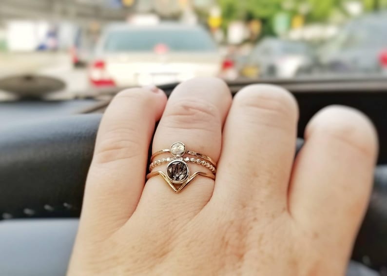 May include: A gold ring with three bands and a clear stone in the centre. The ring is on a person's finger.