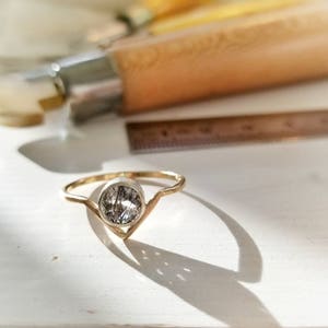 May include: A gold ring with a clear, oval-shaped gemstone set in a V-shaped band.