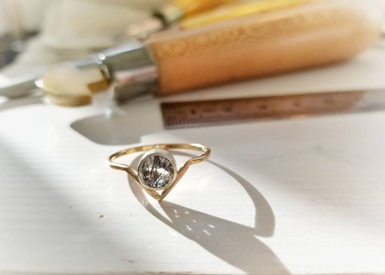 May include: A gold ring with a clear, oval-shaped gemstone set in a V-shaped band.