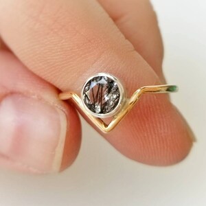 May include: A gold and silver ring with a black and clear gemstone. The ring has a V-shaped band.