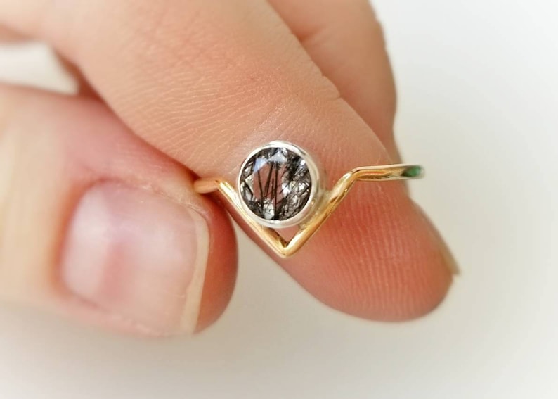 May include: A gold and silver ring with a black and clear gemstone. The ring has a V-shaped band.