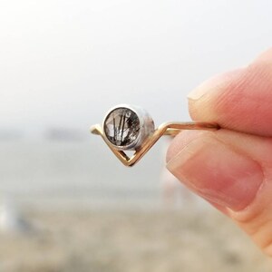 May include: A silver ring with a gold band and a clear gemstone with black inclusions. The ring is shaped like a V.