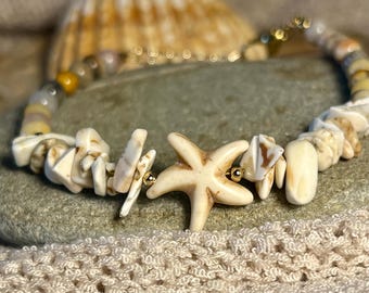 Op de afbeelding: Een schelpenarmband met een zeesterbedel en diverse schelpenfragmenten. De armband heeft een gouden ketting en kleine gouden kralen. De schelpen zijn crème en bruin.