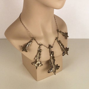 May include: A silver necklace with multiple pendant charms shaped like stylised leaves. The necklace is displayed on a white mannequin bust.