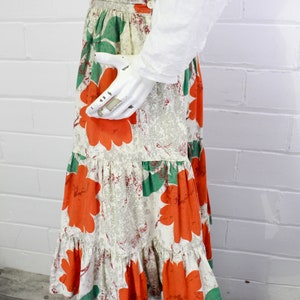 May include: A tiered skirt with a white background and a floral print featuring large orange flowers and green leaves.