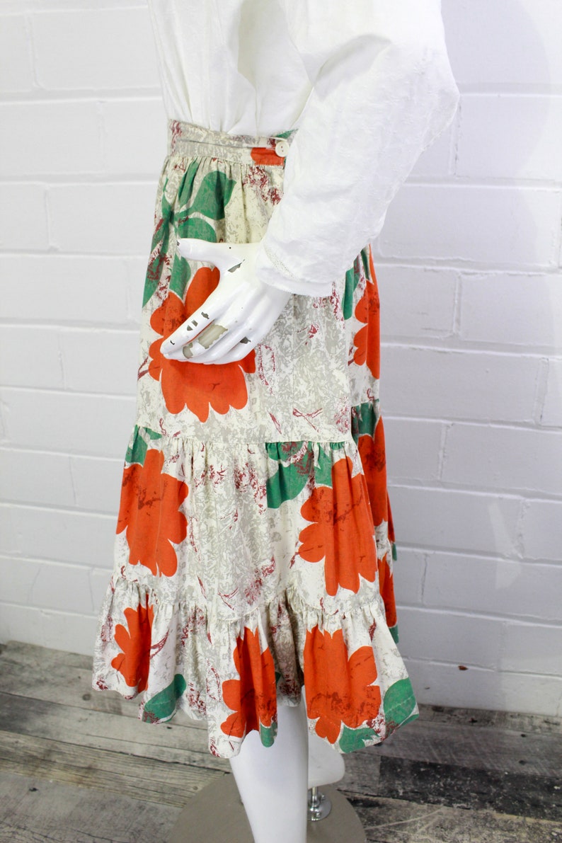 May include: A tiered skirt with a white background and a floral print featuring large orange flowers and green leaves.