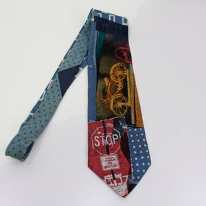 May include: A patterned necktie with a bicycle and stop sign design. The tie features a mix of blue, red, and yellow colors. The tie has a polka dot pattern on the narrow end and a bicycle graphic on the wide end.