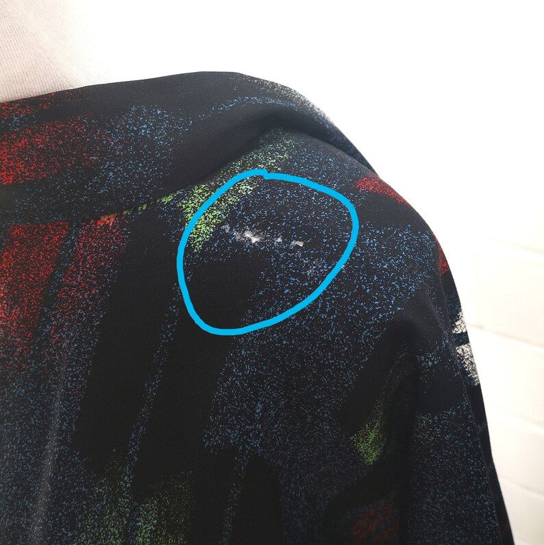 May include: Black fabric with a colorful splatter paint design. The fabric has a slight sheen and a textured surface. There is a small white mark on the fabric.
