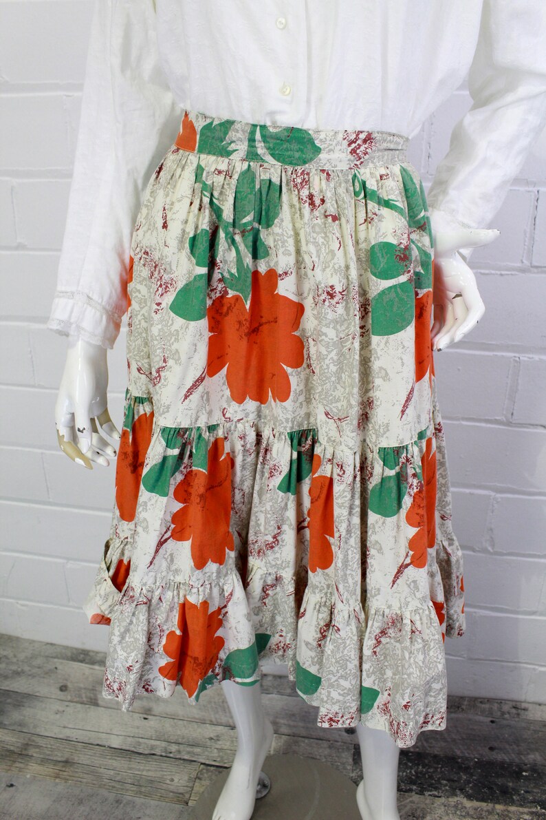 May include: A tiered skirt with a white background and a large floral print in shades of orange and green.