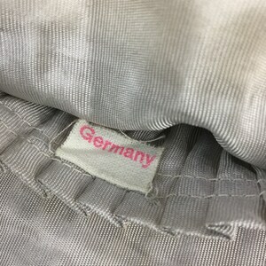 Pode incluir: Close-up de uma etiqueta de tecido branco com a palavra "Germany" impressa em letras cor-de-rosa.