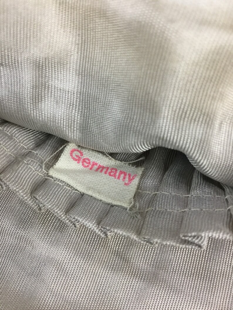 Pode incluir: Close-up de uma etiqueta de tecido branco com a palavra "Germany" impressa em letras cor-de-rosa.