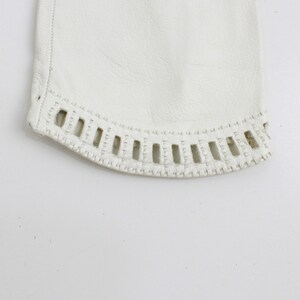 May include: Close-up of the bottom edge of a white leather glove with a decorative stitch pattern.