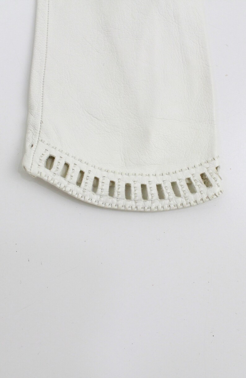 May include: Close-up of the bottom edge of a white leather glove with a decorative stitch pattern.