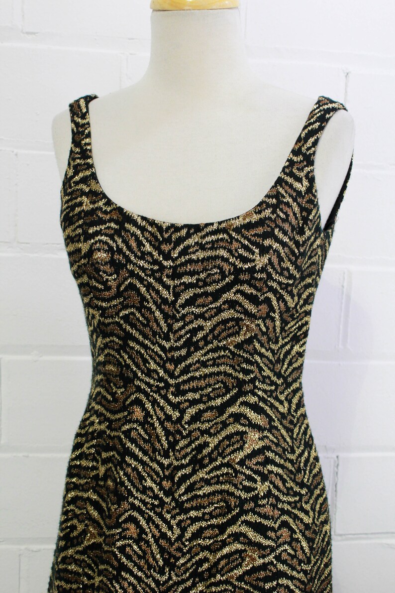 May include: A sleeveless dress with a black and gold zebra print. The dress is made of a sparkly fabric.
