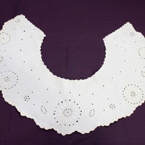 May include: A white cotton collar with a scalloped edge and delicate embroidered floral designs.