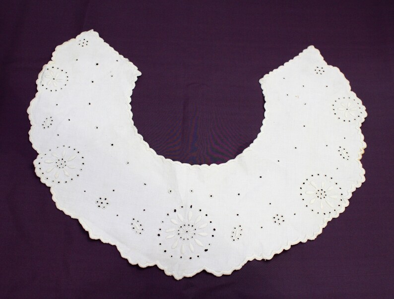 May include: A white cotton collar with a scalloped edge and delicate embroidered floral designs.