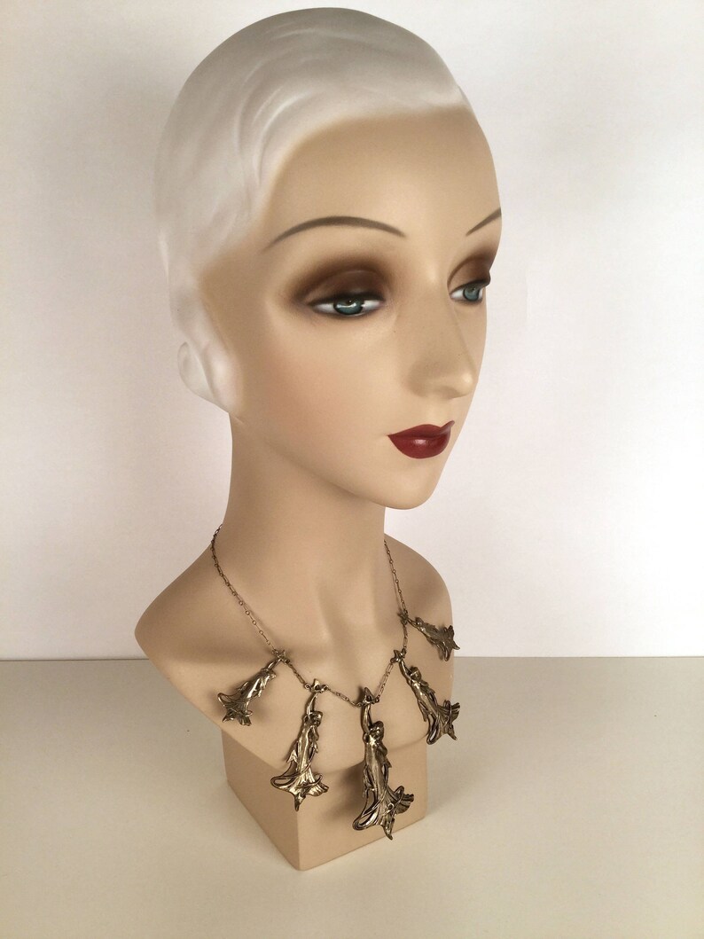 May include: A silver necklace with multiple pendant charms shaped like stylised leaves. The necklace is displayed on a white mannequin bust.