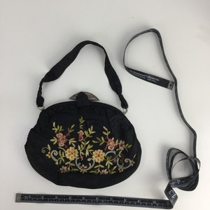 Pode incluir: Uma bolsa de m&atilde;o de cetim preto bordada com um design floral e um fecho de madeira. A bolsa tem uma al&ccedil;a comprida e mede aproximadamente 18 cm de largura.