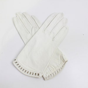 May include: A pair of white leather gloves with a decorative cut-out design on the cuffs.