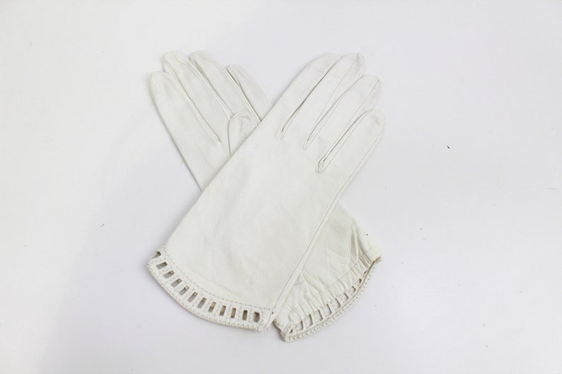 May include: A pair of white leather gloves with a decorative cut-out design on the cuffs.