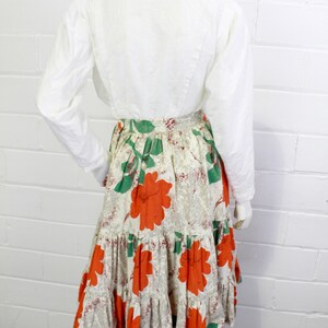 May include: A white long-sleeved blouse with a tiered skirt featuring a floral print in shades of orange, green, and white.