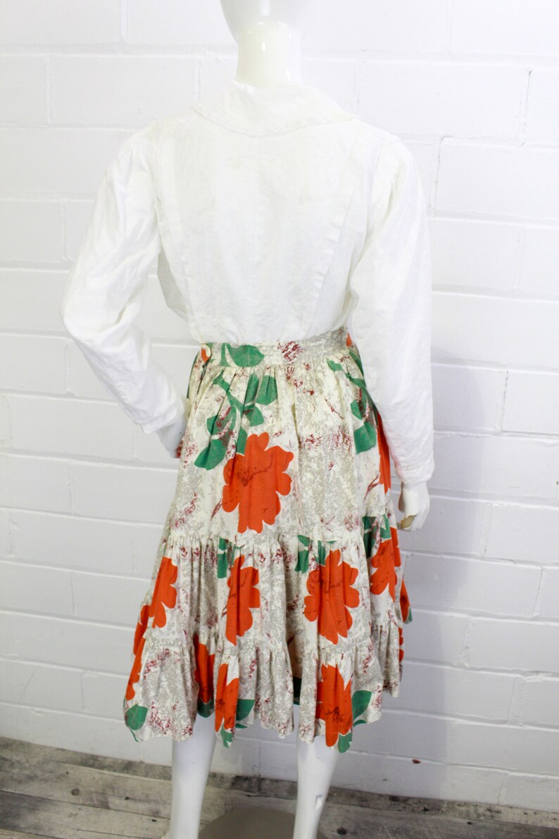 May include: A white long-sleeved blouse with a tiered skirt featuring a floral print in shades of orange, green, and white.