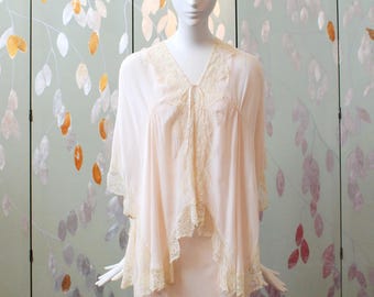 May include: A light peach-colored lingerie set on a mannequin. The set includes a sheer, V-neck top with lace trim and a matching slip. The background features a decorative screen with a floral design.