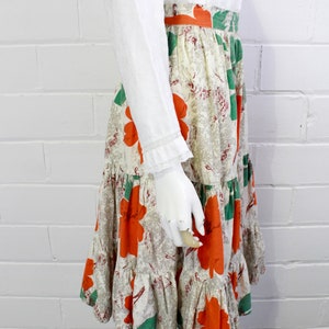 May include: A tiered skirt with a white background and a floral print featuring large orange flowers and green leaves.